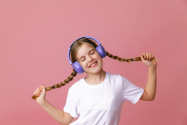 Foto van een schattige grappige jonge tienermeisje in een roze trui koptelefoon dansen genieten van muziek op een achtergrond