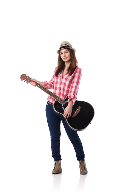 Foto van een schattige jonge vrouw met een geruit overhemd en een hoed die haar gitaar speelt. Ontsproten op een witte achtergrond.