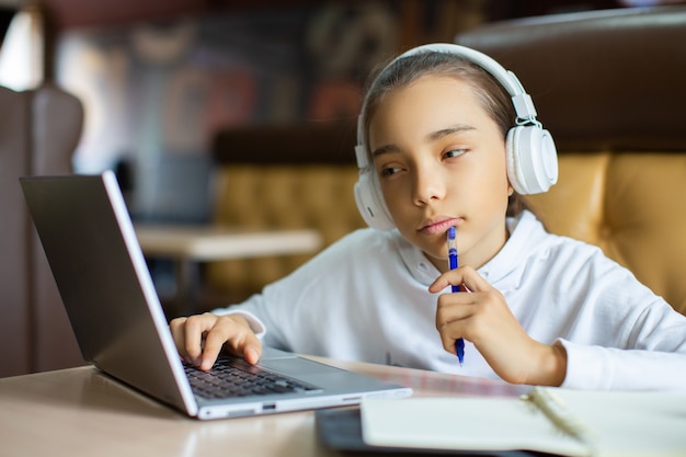 Foto van een tienjarig meisje dat thuis huiswerk maakt voor een laptop-monitormeisje dat online videogesprek voert met leraar