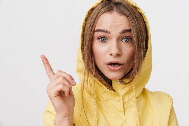 Foto van een verraste blanke vrouw in een regenjas die praat en naar de camera kijkt