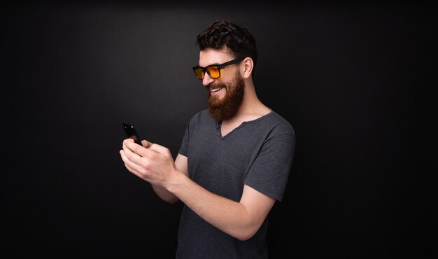 Foto van een vrolijke bebaarde man die smartphone gebruikt en een sms-tekst typt