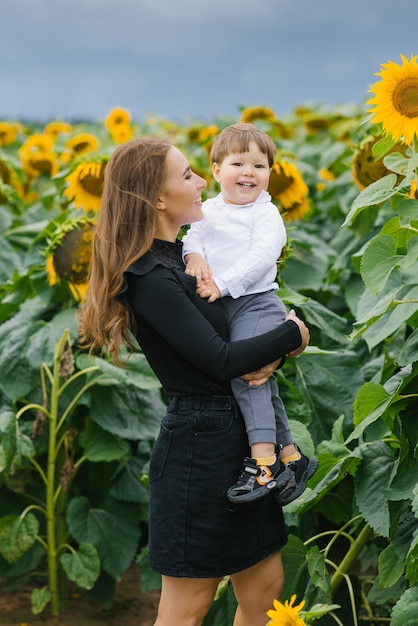 Foto van een vrolijke liefhebbende moeder die plezier heeft met haar kleine kind in een zonnebloemveld