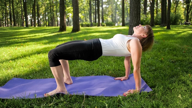 Foto van een vrouw van middelbare leeftijd die yoga of fitness beoefent op vers groen gras in het park. Vrouwelijke lichamelijke en geestelijke gezondheid. Persoon in meditatie en harmonie pf lichaam en ziel