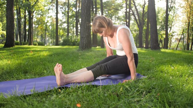 Foto van een vrouw van middelbare leeftijd in sportkleding die buiten yoga beoefent in het park. Vrouw van middelbare leeftijd die zich uitstrekt en mediteert in het bos