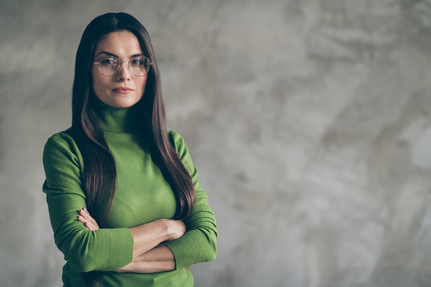 Foto van ernstige zelfverzekerde charmante langharige vrouw met gevouwen handen starend naar je verdacht geïsoleerde muur grijze betonnen achtergrond