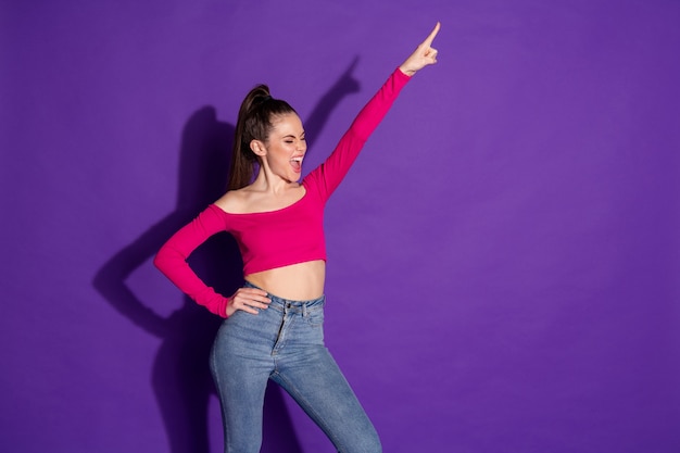 Foto van gekke jongedame hef arm op wijzende vinger omhoog schreeuw draag jeans roze onbedekte schouders top geïsoleerde paarse kleur achtergrond