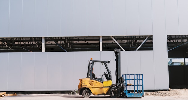 Foto foto van gele heftruck voor het grijze gebouw.