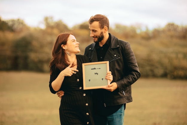 Foto van gelukkige jonge zwangere paar, kijken elkaar en houden een bordje met naam