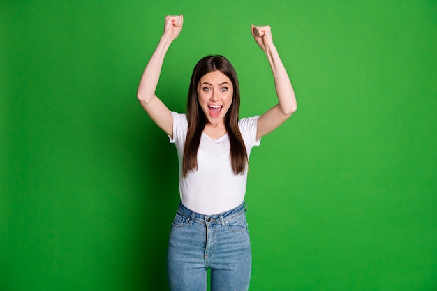 Foto van gelukkige vrouw draagt casual witte t-shirt jeans armen omhoog open mond geïsoleerde groene kleur achtergrond