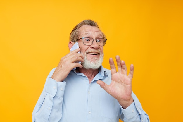 Foto van gepensioneerde oude man grijze baard met bril praten aan de telefoon gele achtergrond