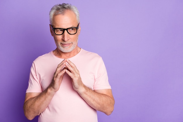 Foto van gepensioneerde oude man houdt armen vast, kijk naar lege ruimte, draag een bril roze t-shirt geïsoleerd paarse kleur achtergrond