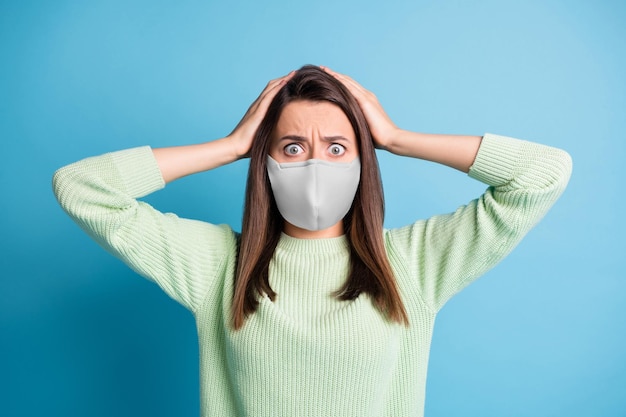 Foto van geschokt bang schattig meisje handen hoofd dragen witte stoffen gezichtsmasker geïsoleerde blauwe kleur achtergrond