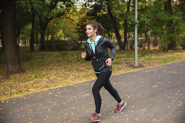 Foto van geweldige jonge mooie fitness vrouw loper buiten in het park loopt.