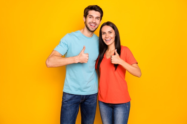 Foto van grappig twee mensen verliefd koppel kerel dame knuffelen duim omhoog vingers uitdrukken overeenkomst slijtage casual blauw oranje t-shirts jeans geïsoleerd over gele kleur muur