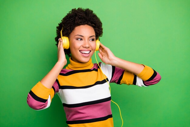 Foto van grappige opgewonden donkere huid dame moderne technologie oortelefoons op oren luisteren populaire liedjes goed humeur dragen casual gestreepte trui