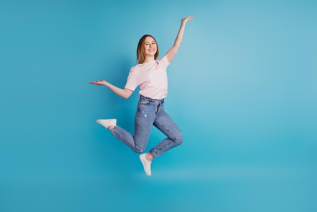 Foto van grappige sportieve dame sprong zorgeloos plezier draag wit t-shirt geïsoleerd op blauwe achtergrond