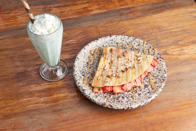 Foto van heerlijke crêpe met aardbei walnoot en gedecoreerd met cajeta geserveerd met vanille milkshake