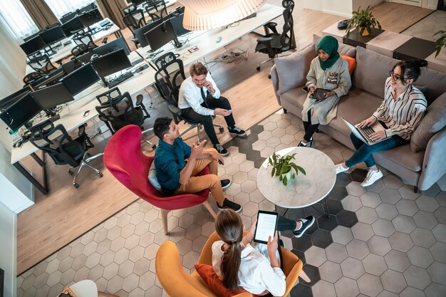 Foto foto van het bovenaanzicht van een multi-etnisch opstartend businessteam met brainstorming in de ontspanningsruimte van een modern kantoorinterieur dat werkt op een laptop en tabletcomputer. foto van hoge kwaliteit