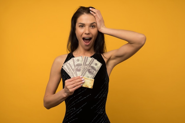 Foto van het tevreden gelukkige jonge vrouw stellen geïsoleerd over gele muur als achtergrond met geld en krediet- of schuldkaart.