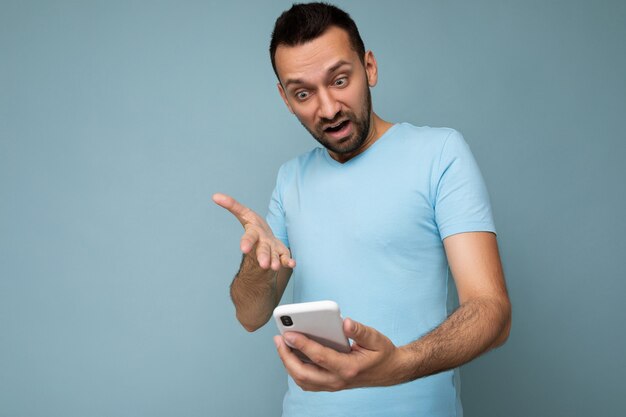 Foto van het vragen van ontevreden knappe jonge man met baard, gekleed in alledaagse blauwe t-shirt geïsoleerd