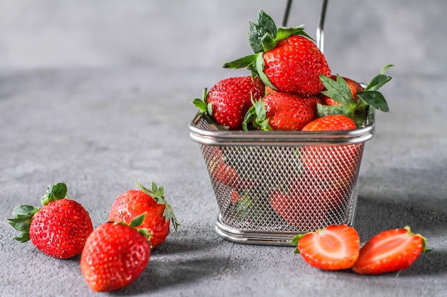 Foto van hoop van verse aardbeien in de mand op rustieke grijze achtergrond. Een bos van rijpe aardbeien in een stalen mand op tafel. Kopieer ruimte. Gezond vers fruit. Biologisch voedsel. Duidelijk voedsel