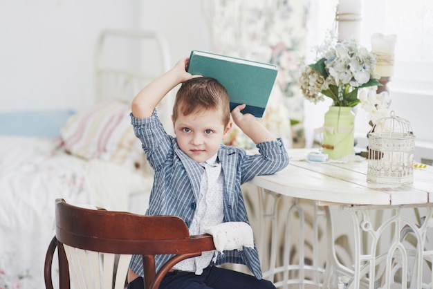 Foto van ijverige schooljongen met boek op zijn hoofd wil niet studeren en naar school gaan. de schooljongen is moe van het maken van huiswerk