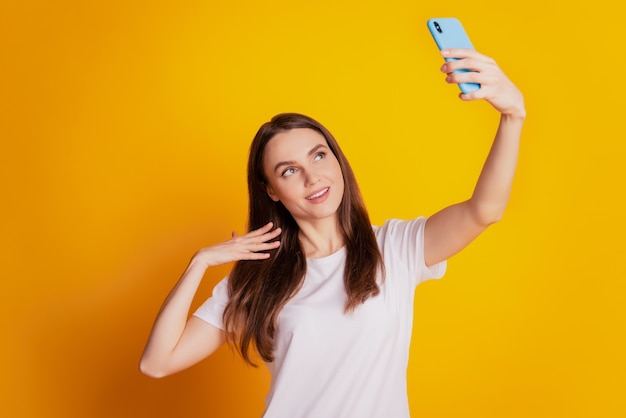 Foto van influencer lady hold phone en neem selfie draag een wit t-shirt poserend op gele achtergrond