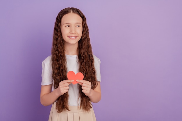 Foto van jong meisje houdt papier valentijn hart kijk lege ruimte geïsoleerd over paarse achtergrond