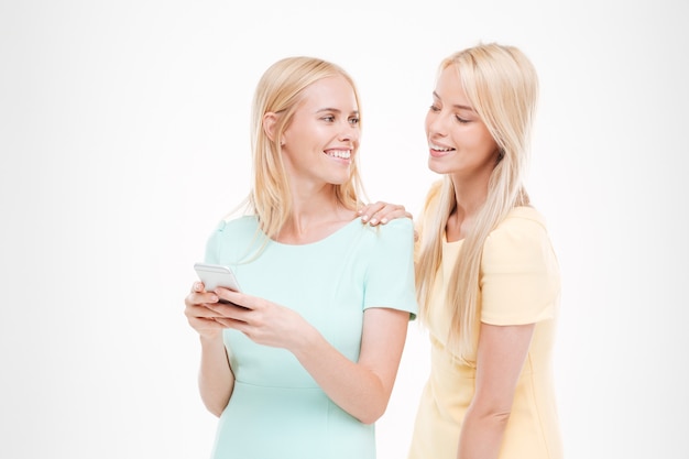 Foto van jonge aantrekkelijke dame die haar telefoon toont aan de vriend. Ge oleerd over witte muur. Elkaar aankijken