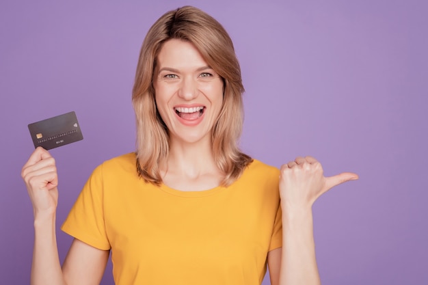 Foto van jonge aantrekkelijke vrouw gelukkig positieve glimlach creditcard punt duim lege ruimte geïsoleerd op violette kleur achtergrond