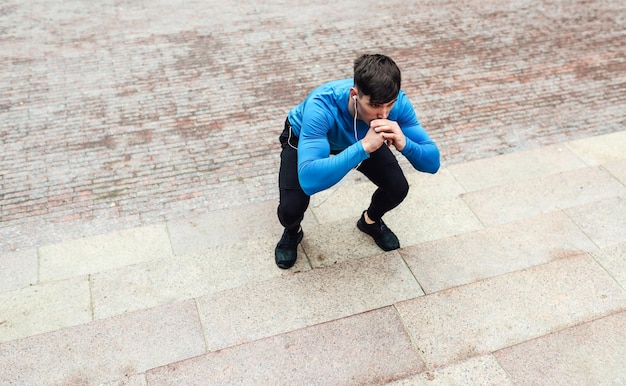 Foto van jonge atletische man die squats uitoefent op de achtergrond van het meer van de stad Fit man doet squats buiten in de ochtend in het park op mistachtergrond Sport levensstijl en mensen concept