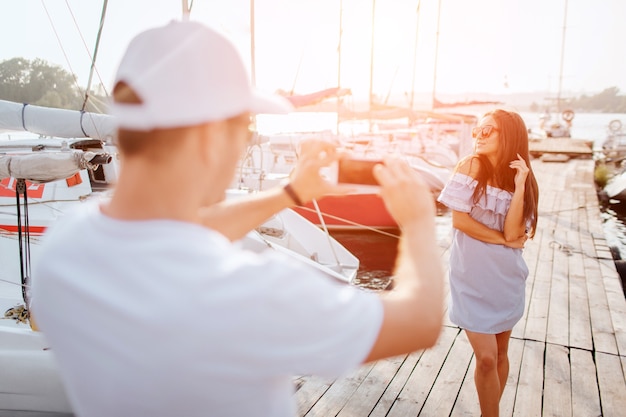 Foto foto van jonge man staat op pier en fotograferen van brunette.