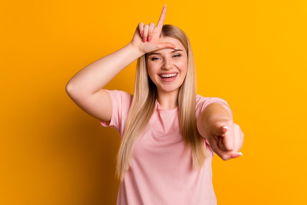 Foto van jonge vrolijke vrouw wijst op vingerlach die spottende pestkop geïsoleerd over gele kleurenachtergrond