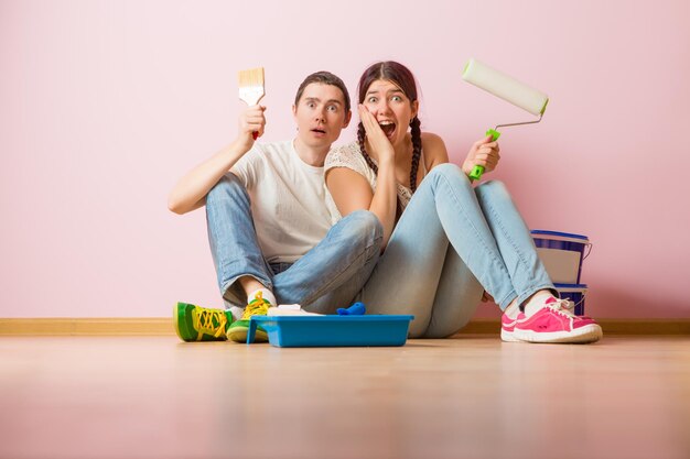 Foto van jonge vrouw en man met verfroller zittend op de vloer