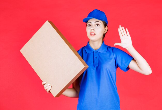 Foto van jonge vrouw in blauwe outfit met kartonnen doos over rode muur.