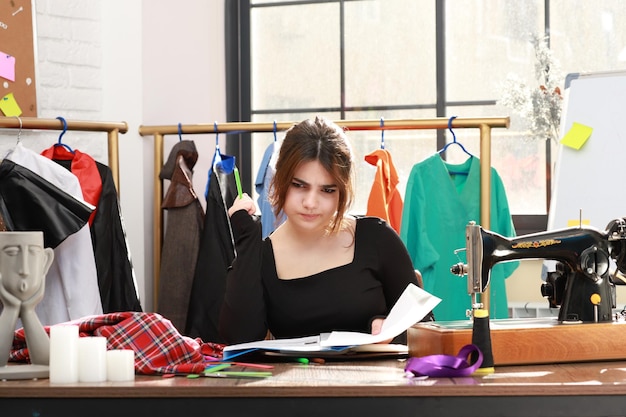 Foto van jonge vrouwelijke kleermaker die in het atelier zit en denkt