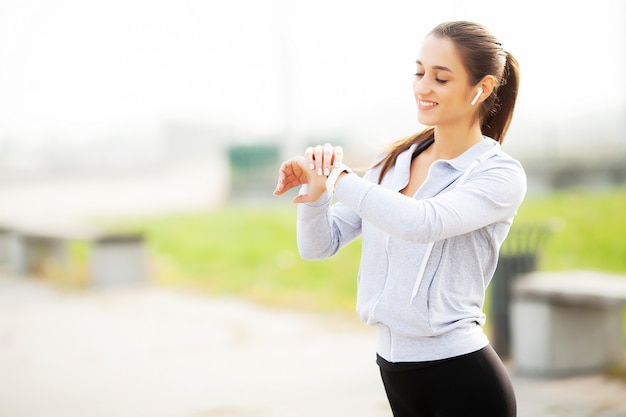 Foto van Joyful Fitness Woman 30s in Sportswear Touching Bluetooth Earpod and Holding Mobile Phone, While Resting in Green Park