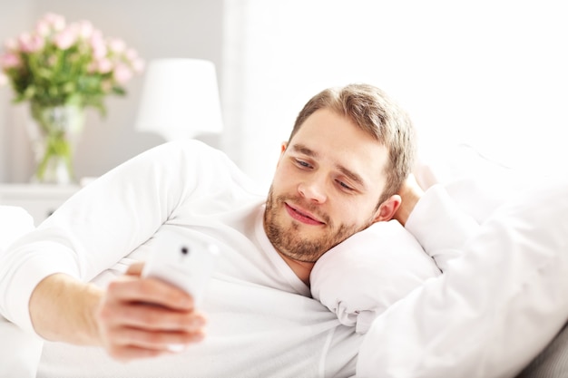 Foto van knappe man liggend in bed met smartphone