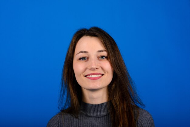 Foto van lachende, vrolijke jonge vrouw in grijze jurk op blauwe muur. Emotioneel portret