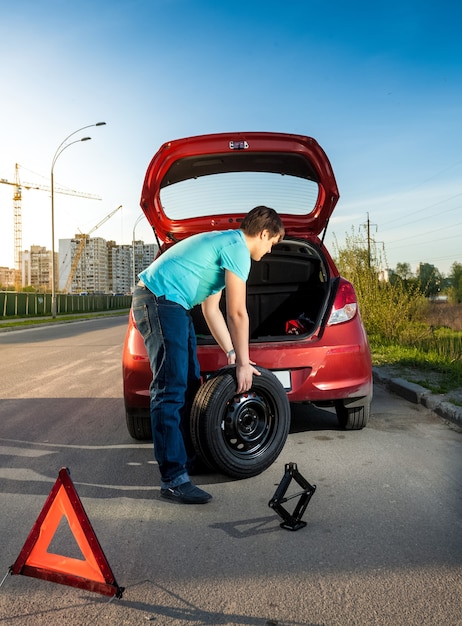 Foto van man die een lek wiel op een kapotte auto verandert