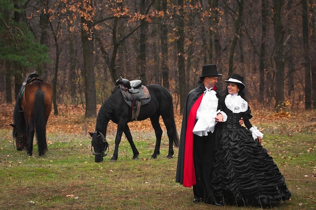 Foto van man en vrouw in prachtige theaterkostuums buiten met paarden