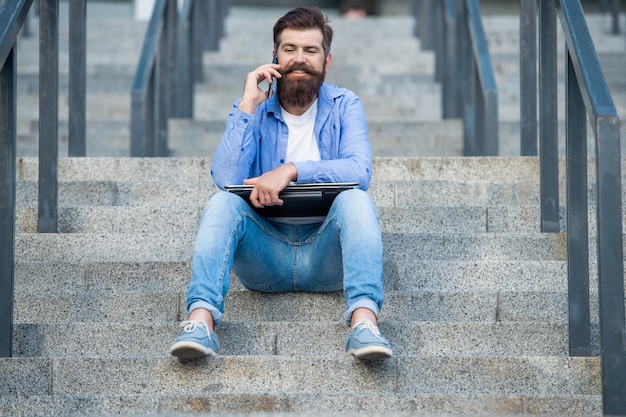 Foto van man praten op smartphone zit op trappen man praat op smartphone buiten