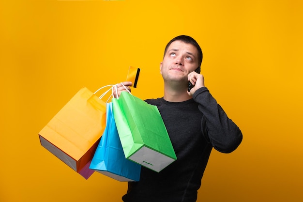 Foto van man shopper met papieren zakken bankkaart en telefoon in de hand