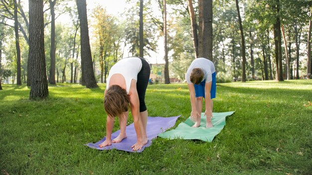 Foto van moeder met haar tienerzoon die yoga asana beoefent op gras in het park. familie die fitness en sport doet in het bos