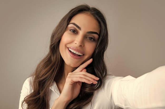 Foto van mooie brunette vrouw lachen en selfie foto nemen op mobiele telefoon geïsoleerd dan grijs