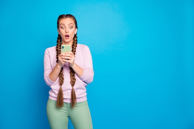 Foto van mooie dame lange vlechten met telefoonhanden lezen ongelooflijk slecht nieuws afkeer op post dragen casual pullover broek geïsoleerde blauwe kleur achtergrond