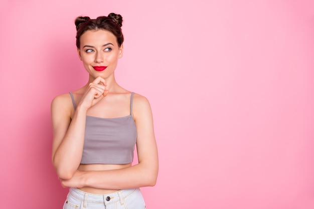 Foto van mooie jonge dame mooie broodjes rode pommade arm op kin op zoek dromerige lege ruimte dragen casual grijze korte top geïsoleerde roze kleur