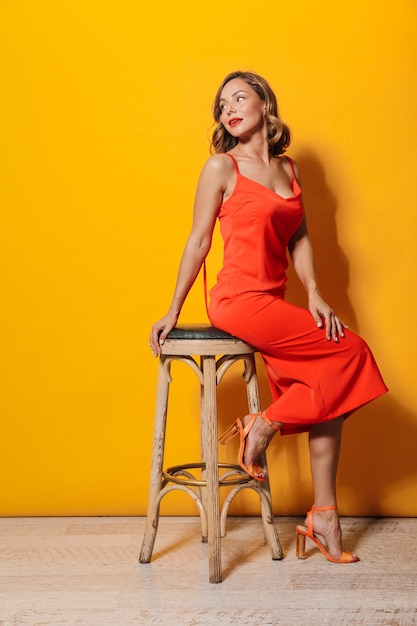 Foto van mooie jonge vrouw met rode jurk zittend op stoel geïsoleerd