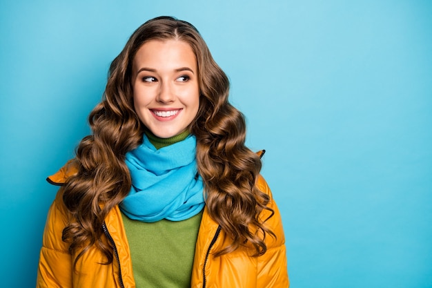 Foto van mooie krullende dame op zoek naar kant lege ruimte zonnige winterdag straat kijken dragen casual gele warme overjas blauwe sjaal groene trui geïsoleerde blauwe kleur muur