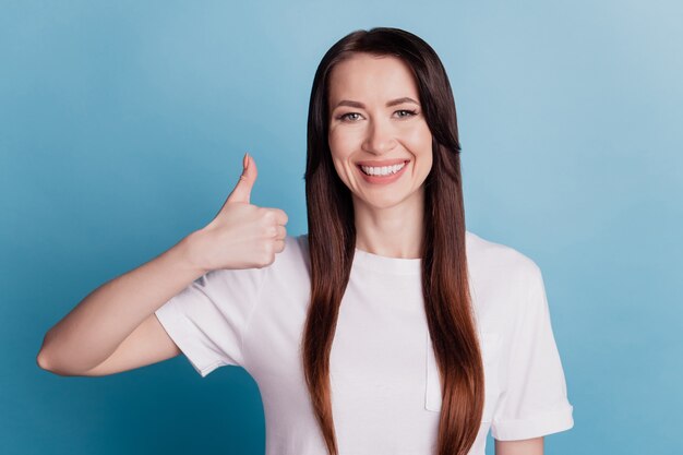 Foto van mooie lachende jonge vrouw geven duimen omhoog geïsoleerd op blauwe achtergrond